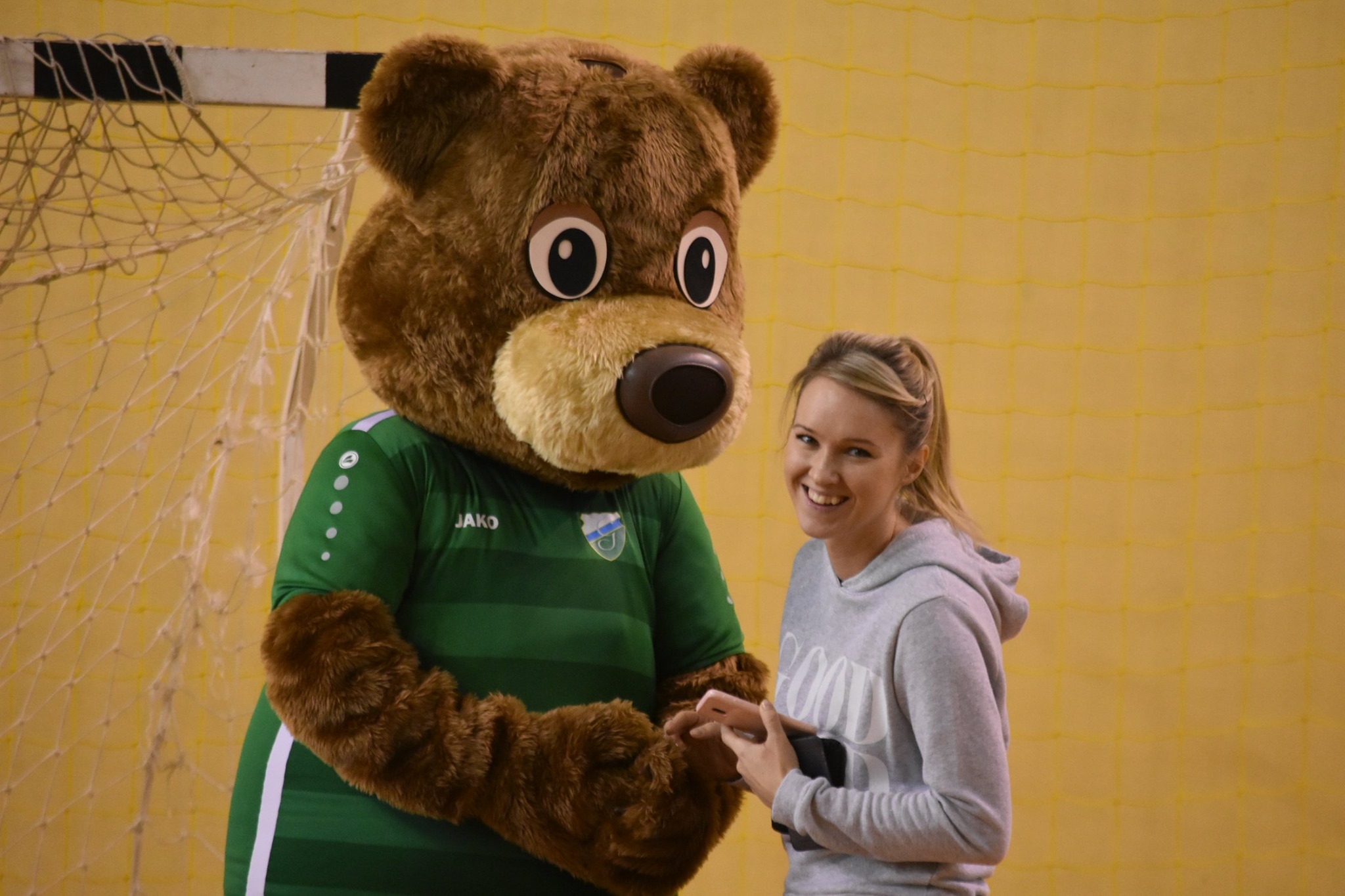 Na fotografii widnieje przebranie za misia z futerka w towarzystwie kobiety. W tle bramka do piłki ręcznej.
